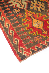Detalle lateral de alfombra con borde geométrico, pequeños motivos florales y diseño central en tonos rojo y negro.
