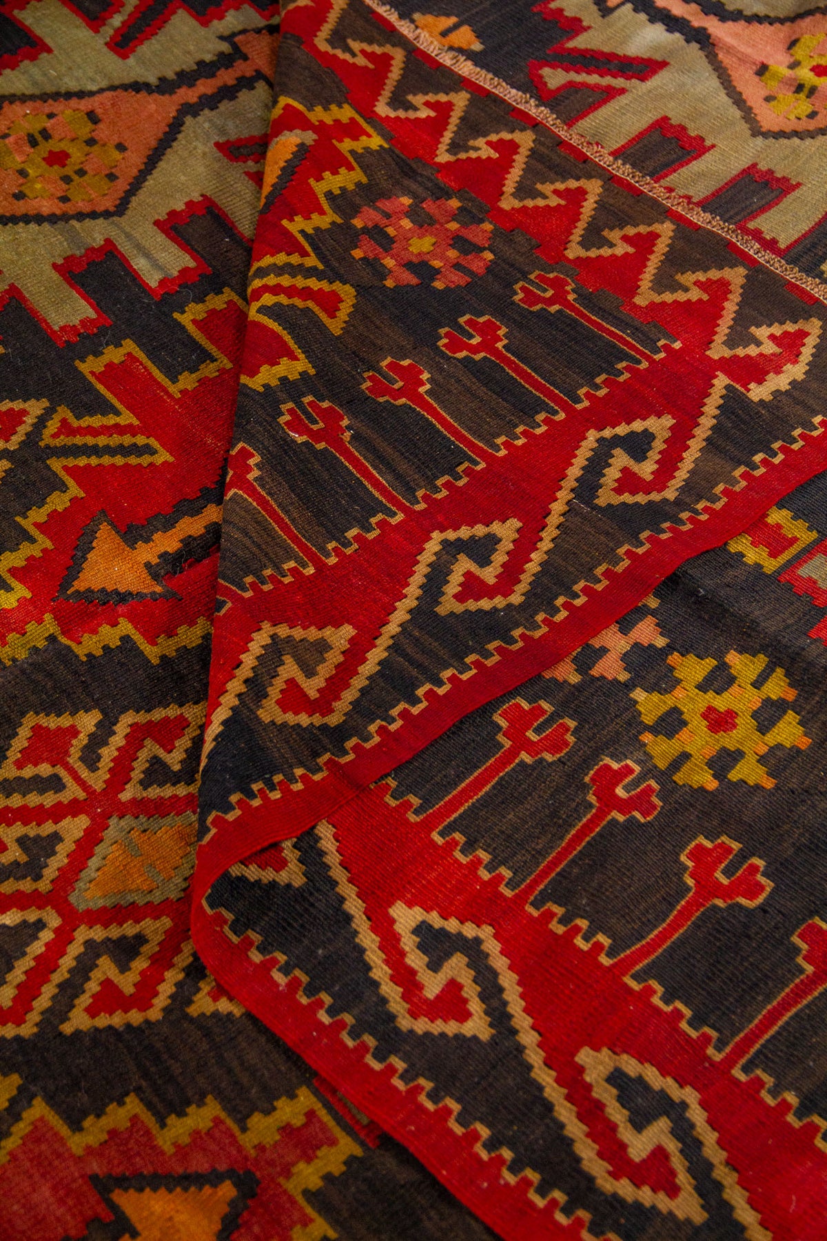 Detalle de alfombra doblada que resalta la guarda geométrica y los colores intensos del tejido artesanal.