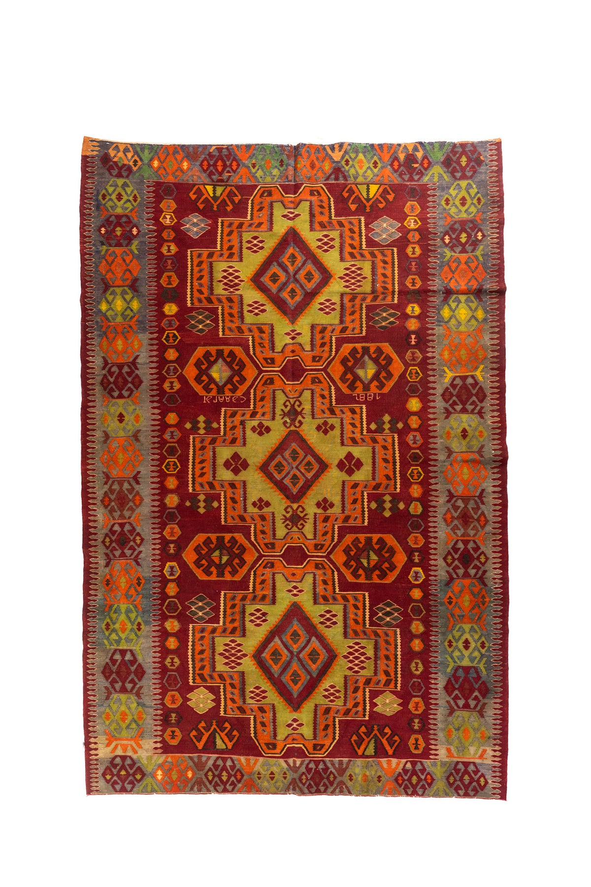 Alfombra rectangular de estilo geométrico tribal en tonos rojo, naranja, dorado y gris, con tres grandes medallones centrales y guardas laterales multicolor.