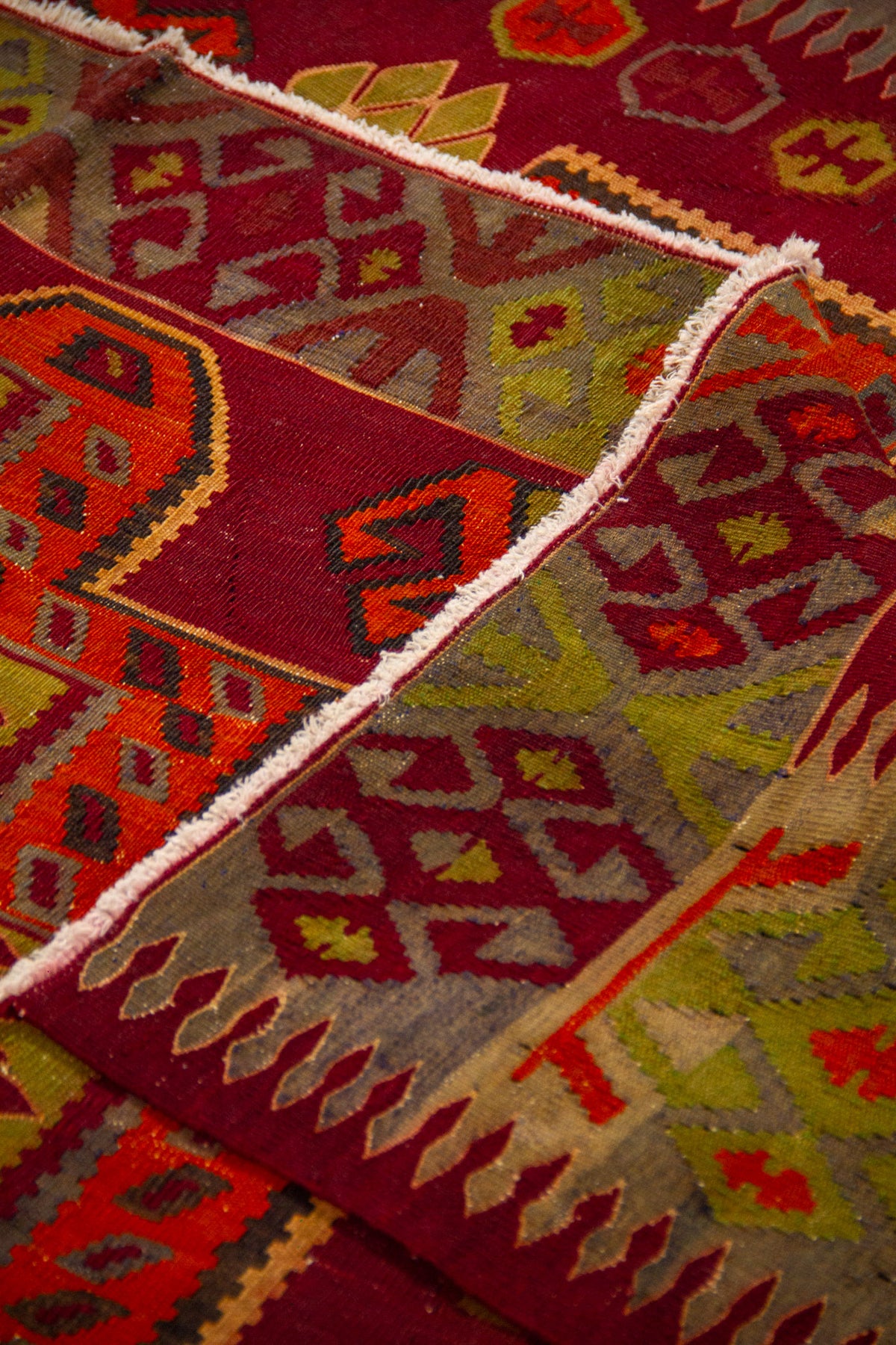 Detalle de alfombra doblada que muestra la textura del tejido y la composición geométrica del borde en tonos cálidos 