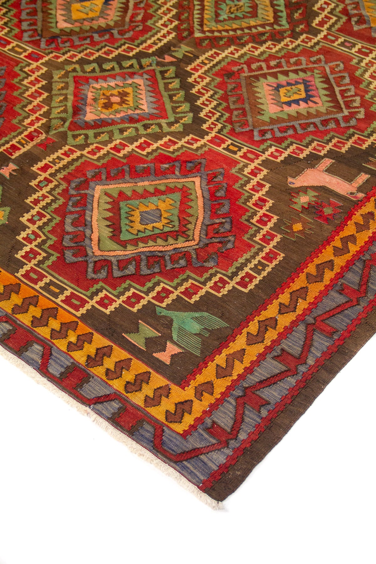 Detalle de alfombra artesanal con rombos escalonados multicolor y borde geométrico en tonos cálidos