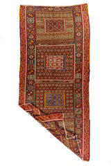 Alfombra artesanal geométrica vista en perspectiva con una esquina doblada que muestra su textura, tejido y reverso