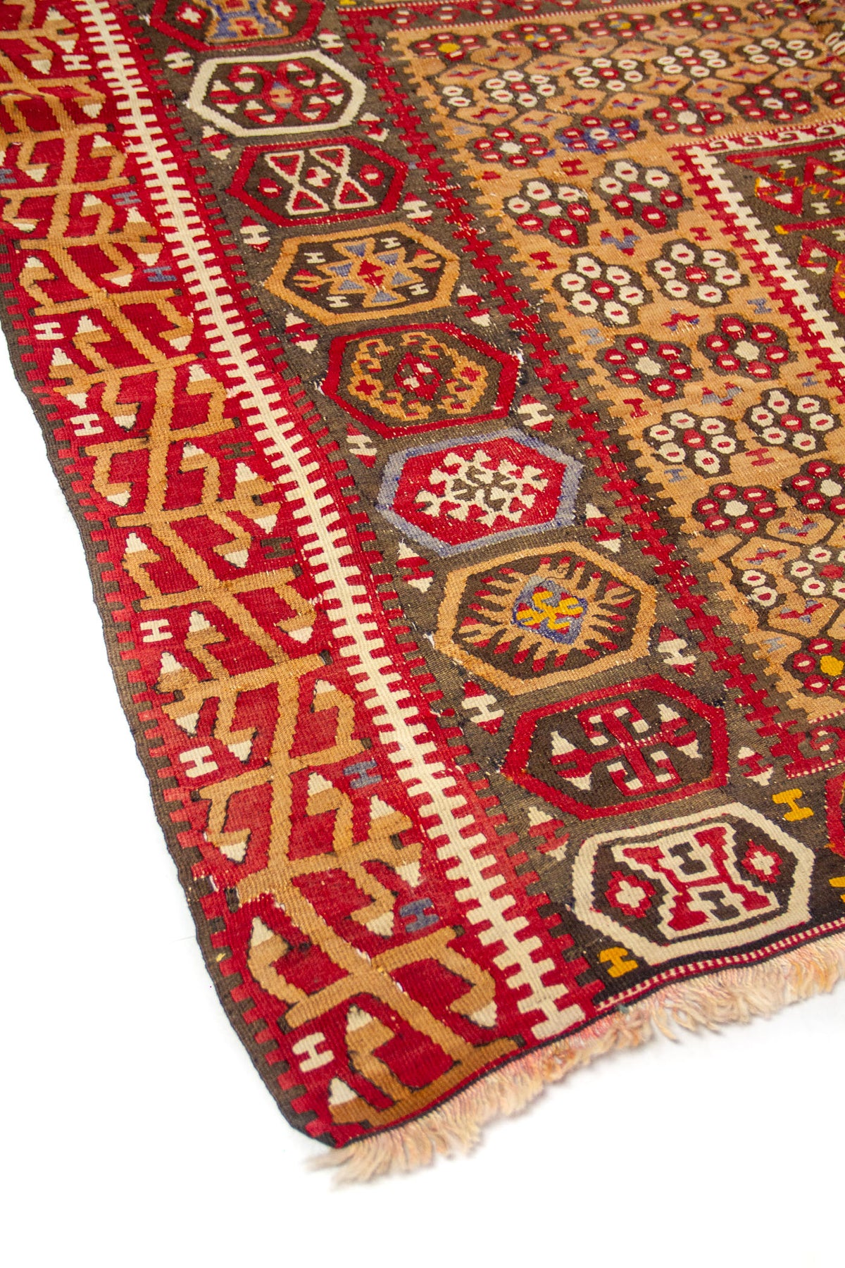 Detalle lateral de alfombra artesanal con guarda roja, motivos geométricos hexagonales y flecos en un extremo