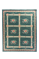 Alfombra rectangular en tono verde y azul con diseño de cuadrícula y ramilletes florales en el centro