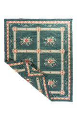 Alfombra verde y azul con esquina doblada que muestra el diseño floral y su acabado textil