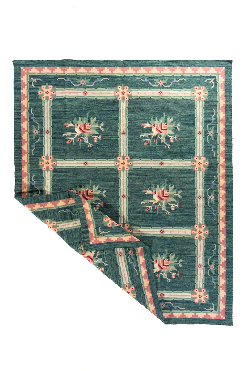Alfombra verde y azul con esquina doblada que muestra el diseño floral y su acabado textil