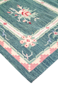 Detalle de esquina de alfombra con fondo verde y azul, líneas geométricas y acentos en rosa y blanco suave