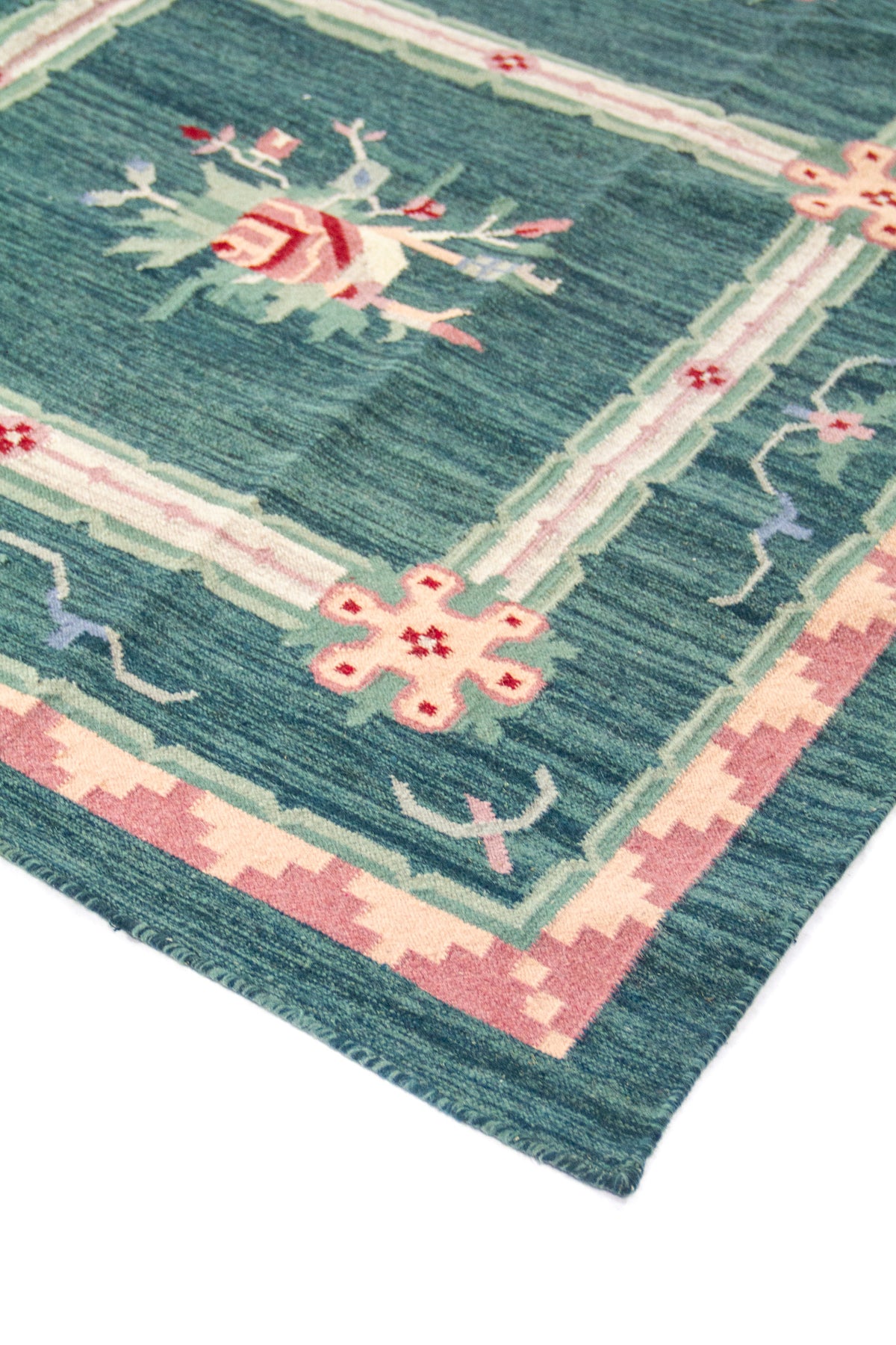 Primer plano de alfombra con motivo floral central y patrón geométrico en tonos verde, rosa y blanco suave