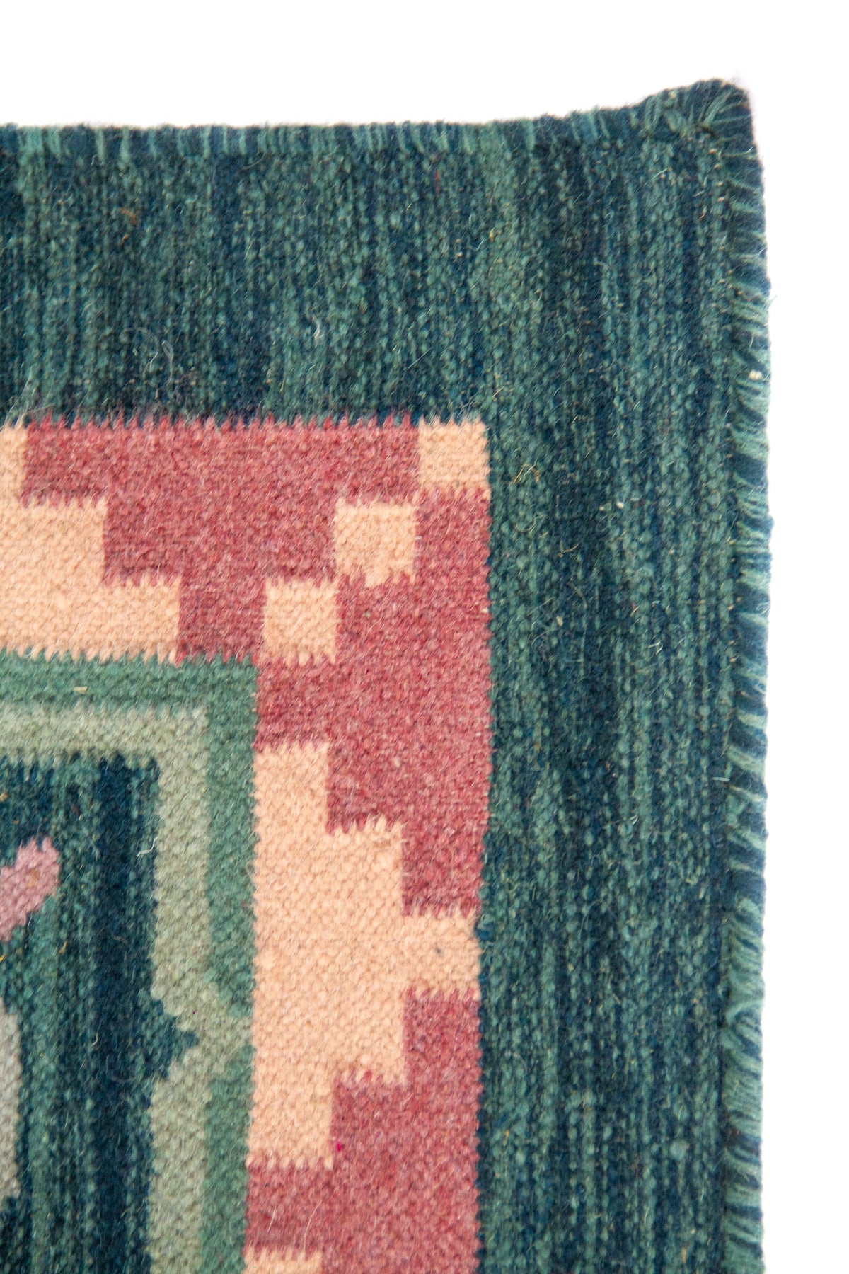 Detalle del borde de alfombra con guarda geométrica en rosa y fondo verde y azul