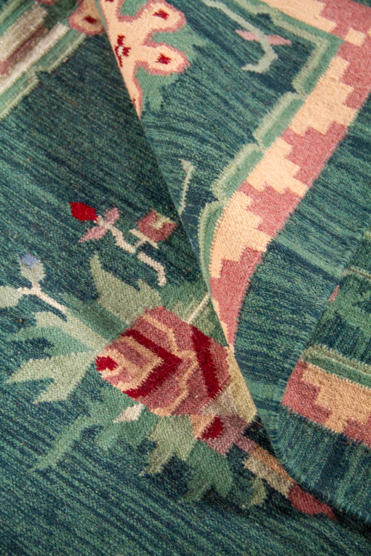 Detalle de alfombra doblada mostrando la textura tejida y el diseño floral en tonos suaves