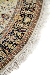 Detalle del borde curvo de alfombra ovalada con guarda negra floral, fondo beige y flecos claros alrededor