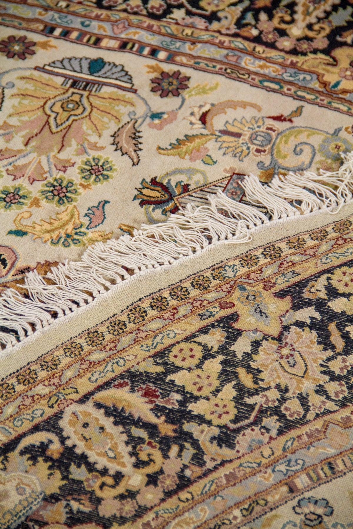 Detalle de alfombra doblada mostrando textura, reverso del tejido y composición decorativa en tonos beige, negro y dorado