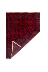 Alfombra Persa Afgan roja con esquina doblada mostrando reverso y flecos