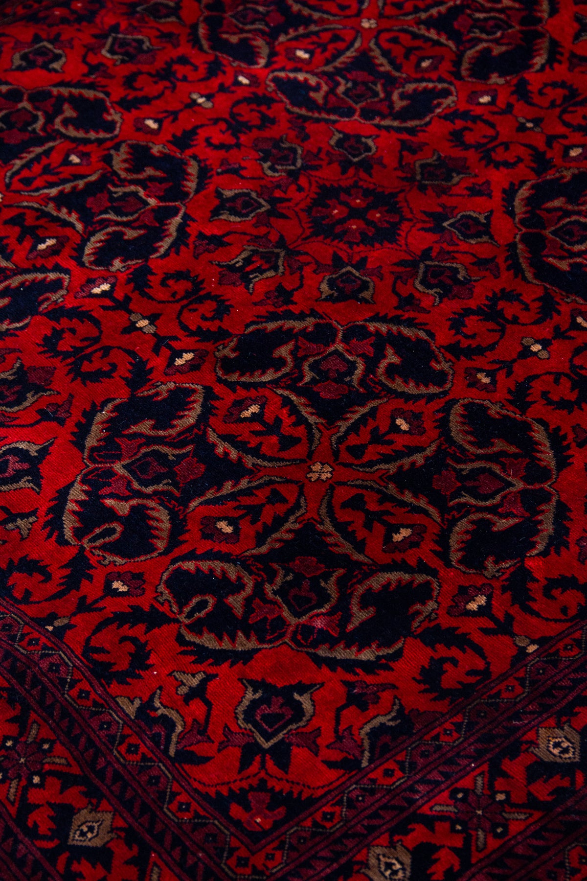 Detalle del diseño floral de alfombra Persa Afgan en tonos rojos y azul oscuro