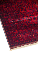 Primer plano del borde de una alfombra oriental roja con patrón geométrico repetitivo y guarda decorativa en tonos rojo y azul marino.