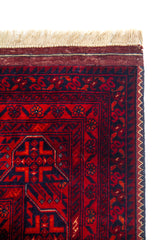 Detalle de esquina superior de alfombra roja con flecos beige y finos patrones geométricos de inspiración tribal.