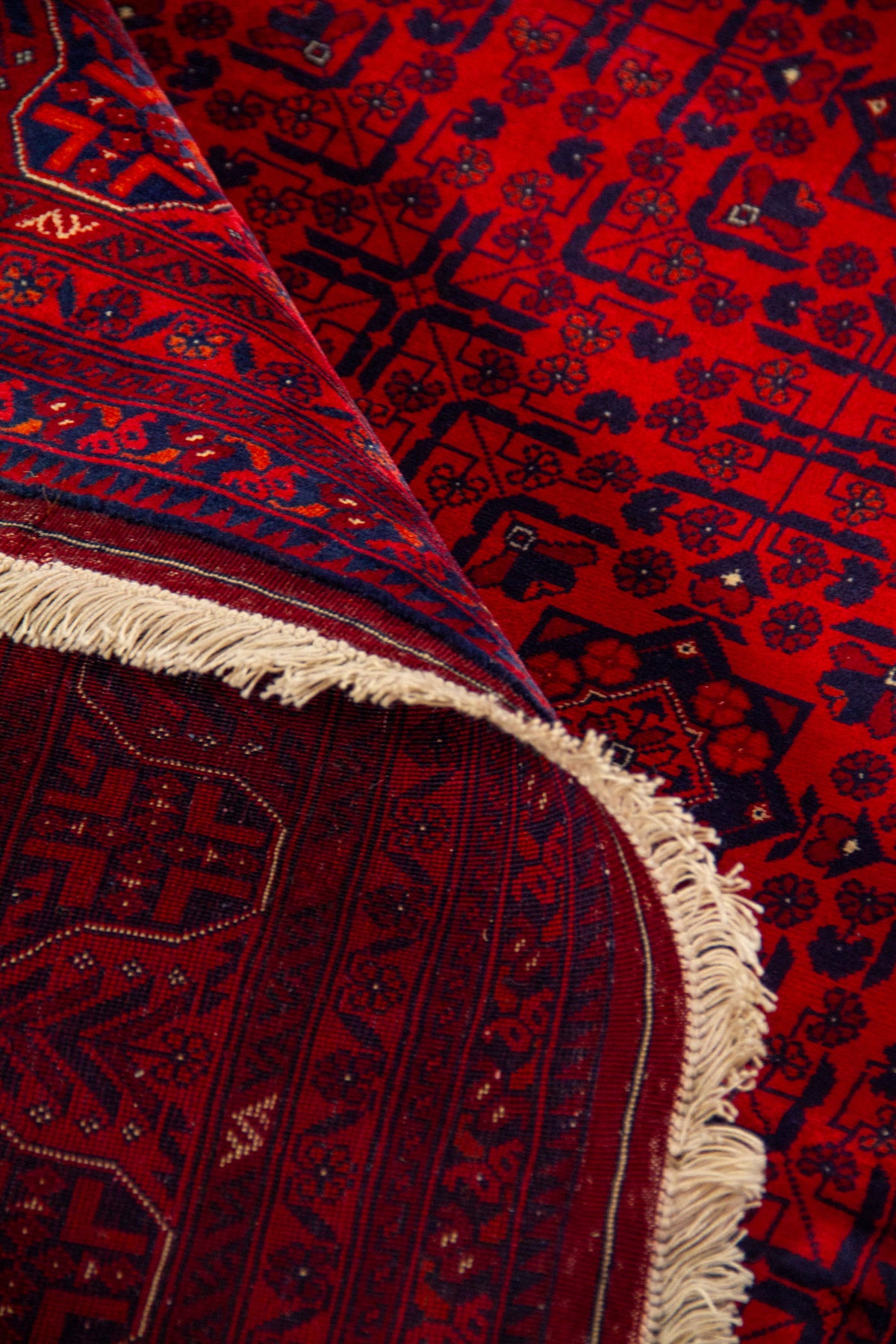 Alfombra roja enrollada mostrando la textura, el reverso tejido y los motivos geométricos tradicionales en rojo y azul oscuro.