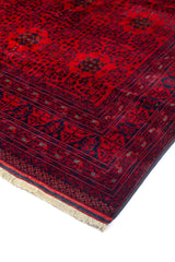 Primer plano de borde de alfombra oriental roja con diseño geométrico repetitivo, guardas decorativas y contraste en tonos rojo y azul marino.