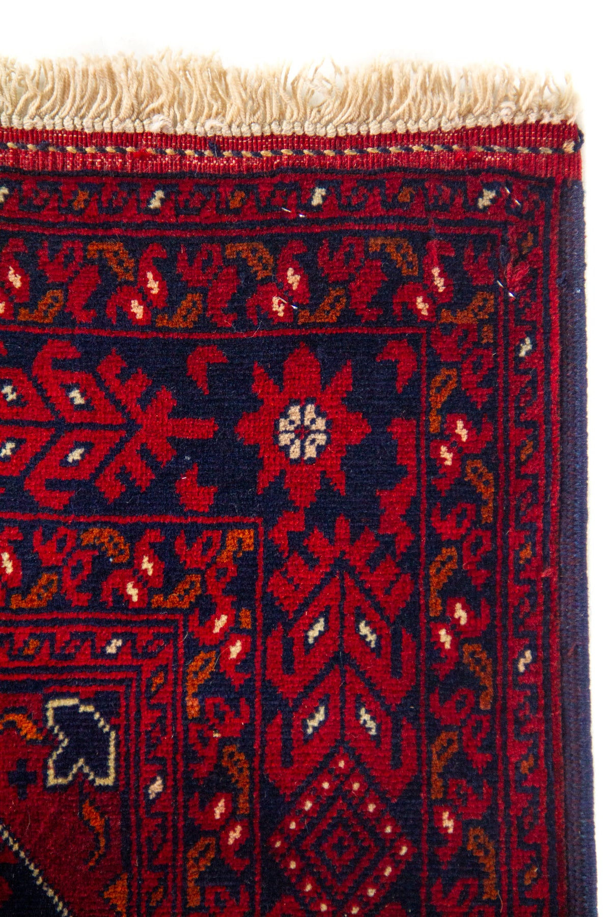 Detalle del borde superior de una alfombra con guarda decorativa geométrica, fondo azul oscuro y flecos claros.
