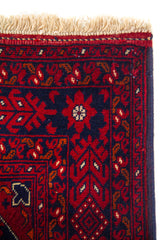 Detalle del borde superior de una alfombra con guarda decorativa geométrica, fondo azul oscuro y flecos claros.
