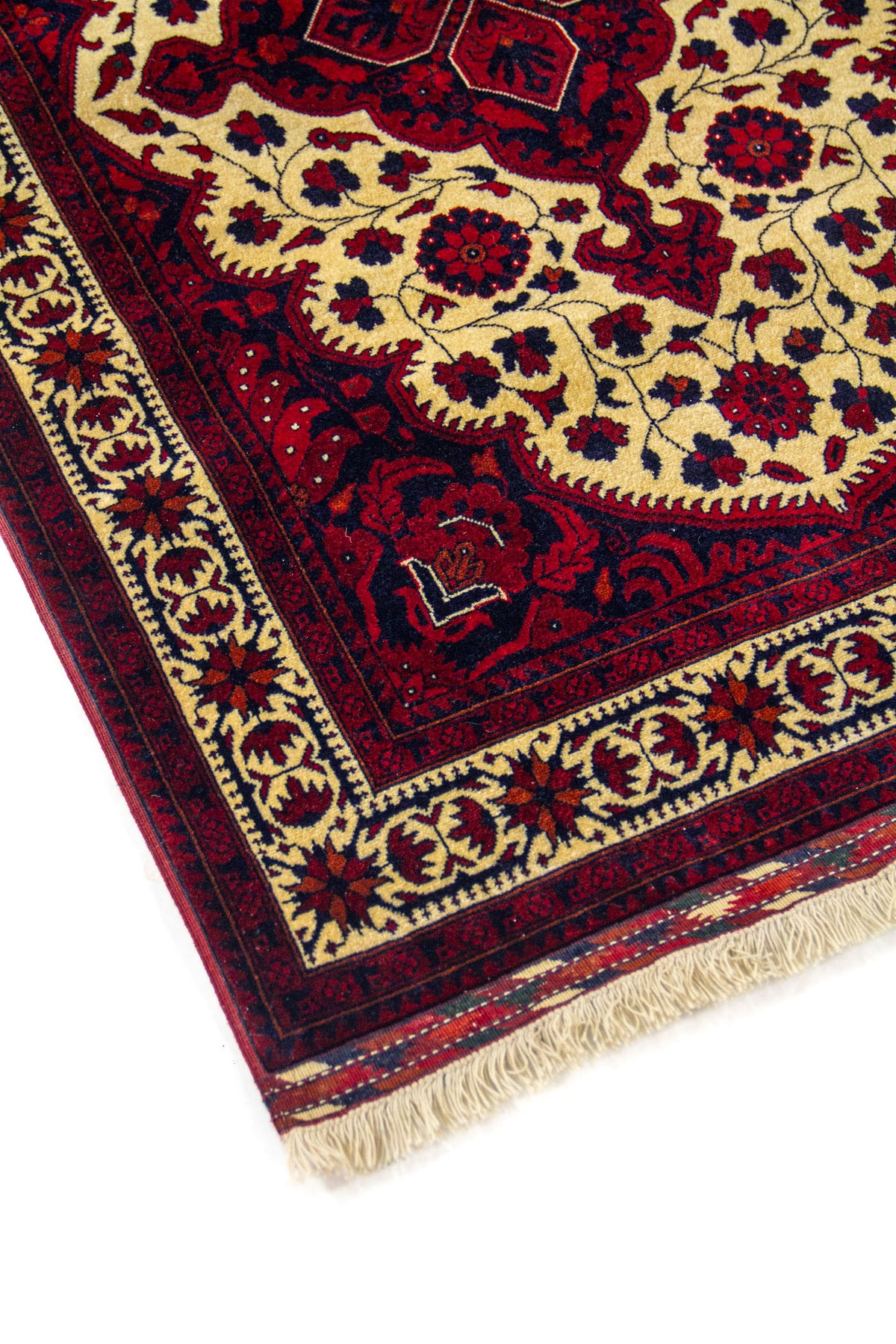 Detalle en esquina de alfombra con medallón amarillo claro, bordes decorativos en rojo oscuro y azul marino, y flecos visibles en un extremo.