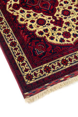 Detalle en esquina de alfombra con medallón amarillo claro, bordes decorativos en rojo oscuro y azul marino, y flecos visibles en un extremo.