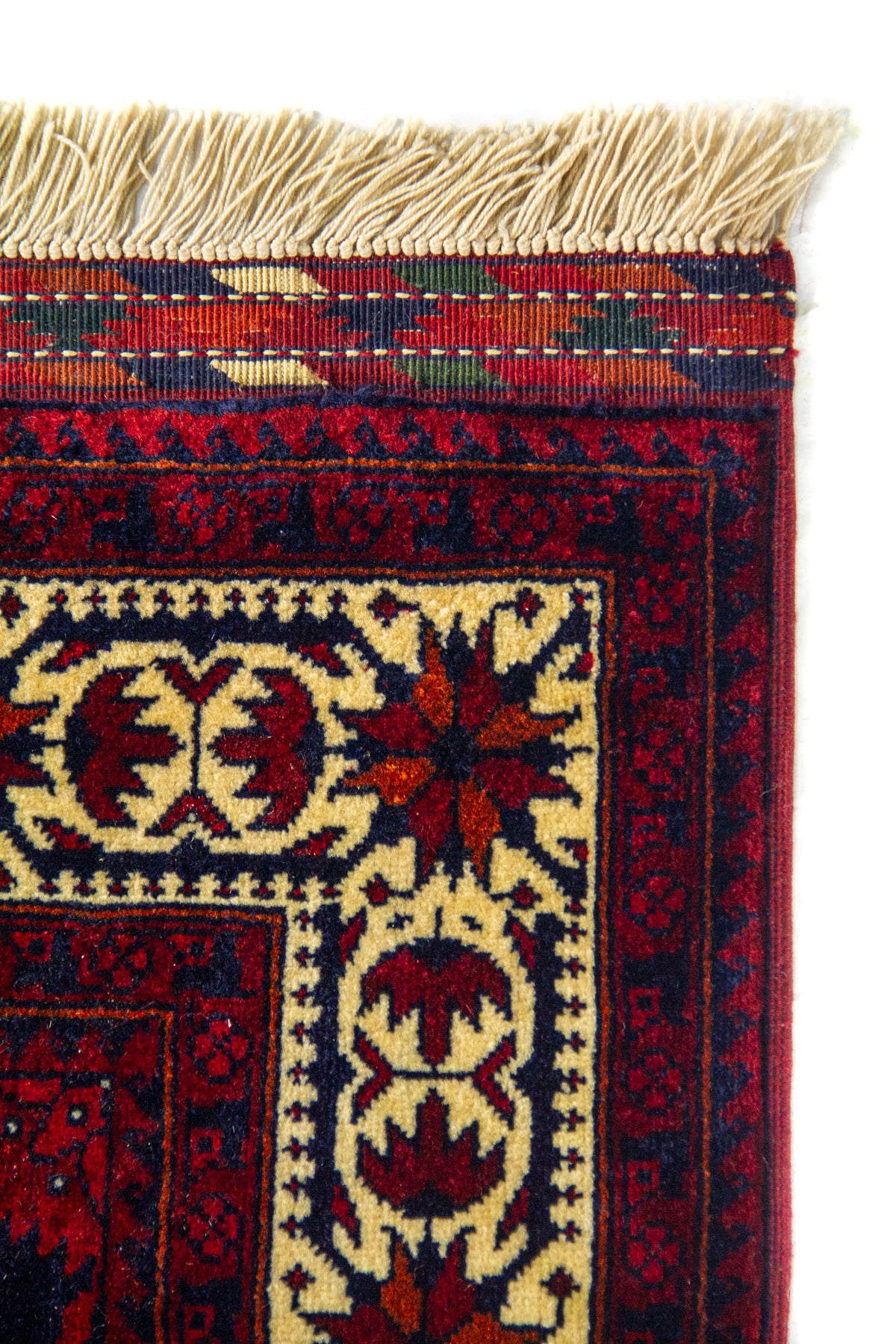 Detalle del borde superior de una alfombra oriental con guarda amarillo claro decorada, flecos beige y combinación de colores rojo y azul.