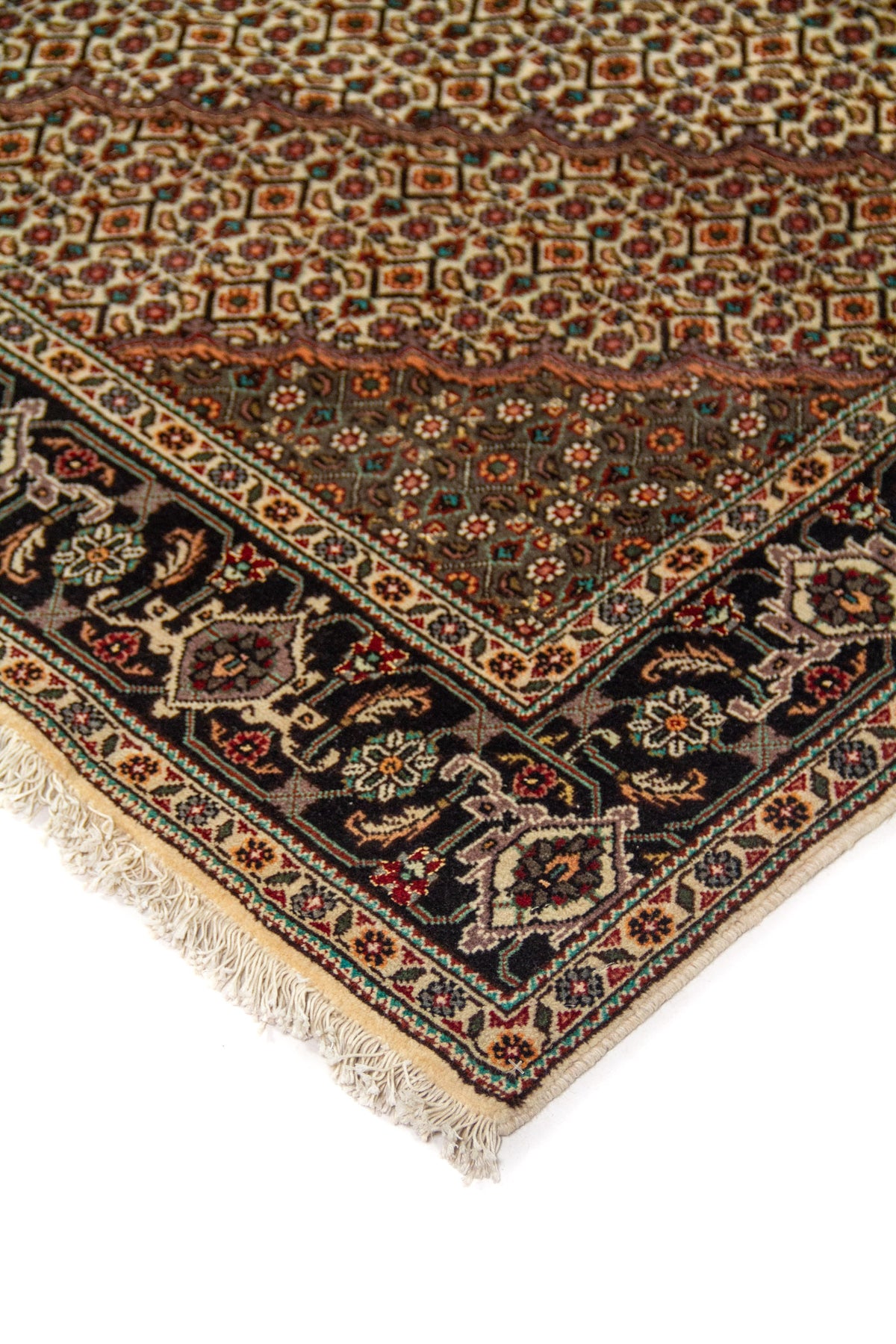 Detalle de esquina de alfombra oriental con fondo blanco suave, motivos geométricos, guarda negra floral y flecos claros