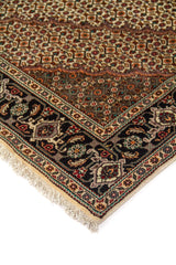 Detalle de esquina de alfombra oriental con fondo blanco suave, motivos geométricos, guarda negra floral y flecos claros