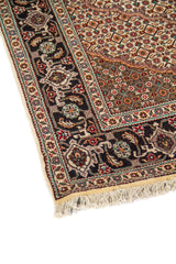 Primer plano del borde de alfombra clásica con guarda negra ornamentada y patrón geométrico en tonos beige, rojo oscuro y celeste