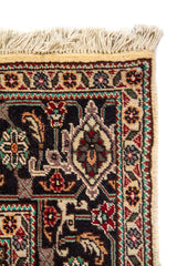 Detalle de esquina superior de alfombra con flecos, borde decorativo oscuro y finos motivos florales geométricos