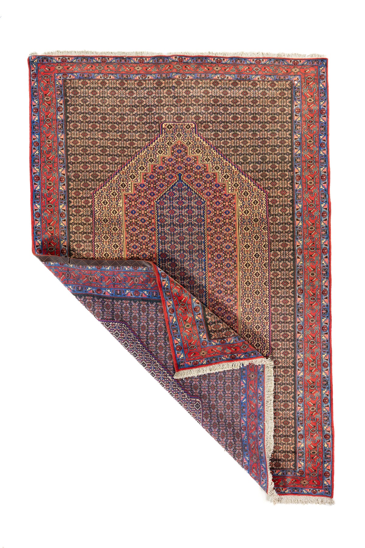 Alfombra clásica rectangular con una esquina doblada que muestra el reverso del tejido, los flecos y el detalle del borde geométrico