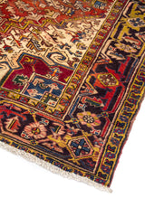 Primer plano de alfombra geométrica en tonos rojo, beige y azul con figuras simétricas y borde decorativo oscuro