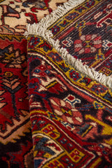 Detalle de alfombra doblada mostrando la textura del tejido, el reverso y los motivos geométricos en tonos rojo, azul y beige.