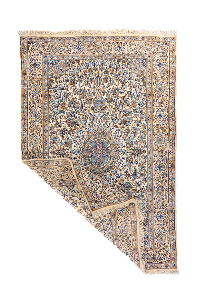 Alfombra oriental en tonos blanco suave y azul con una esquina doblada, mostrando el reverso del tejido y los flecos en uno de sus extremos.