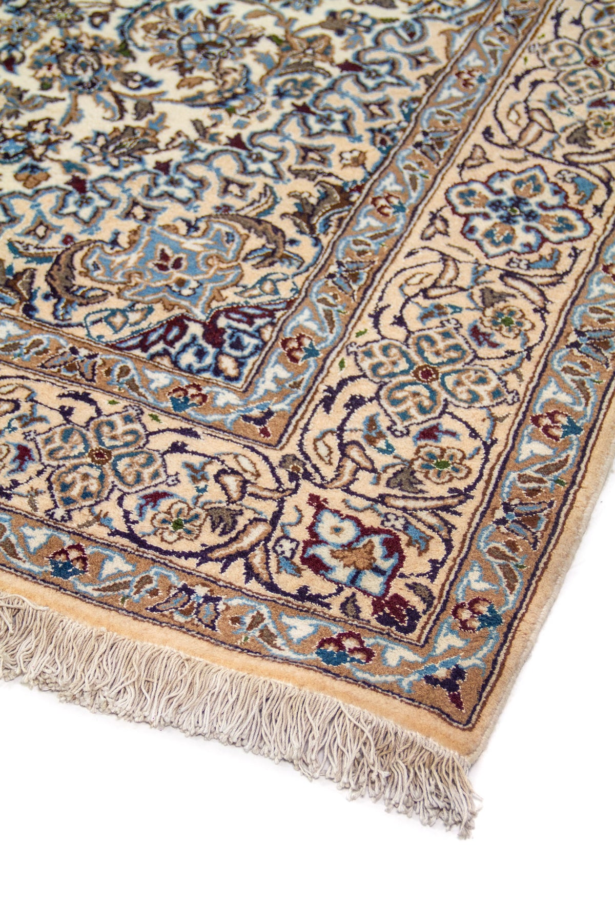 Detalle de esquina de alfombra clásica con motivos florales en azul, celeste y beige sobre fondo blanco suave, terminada con flecos claros.