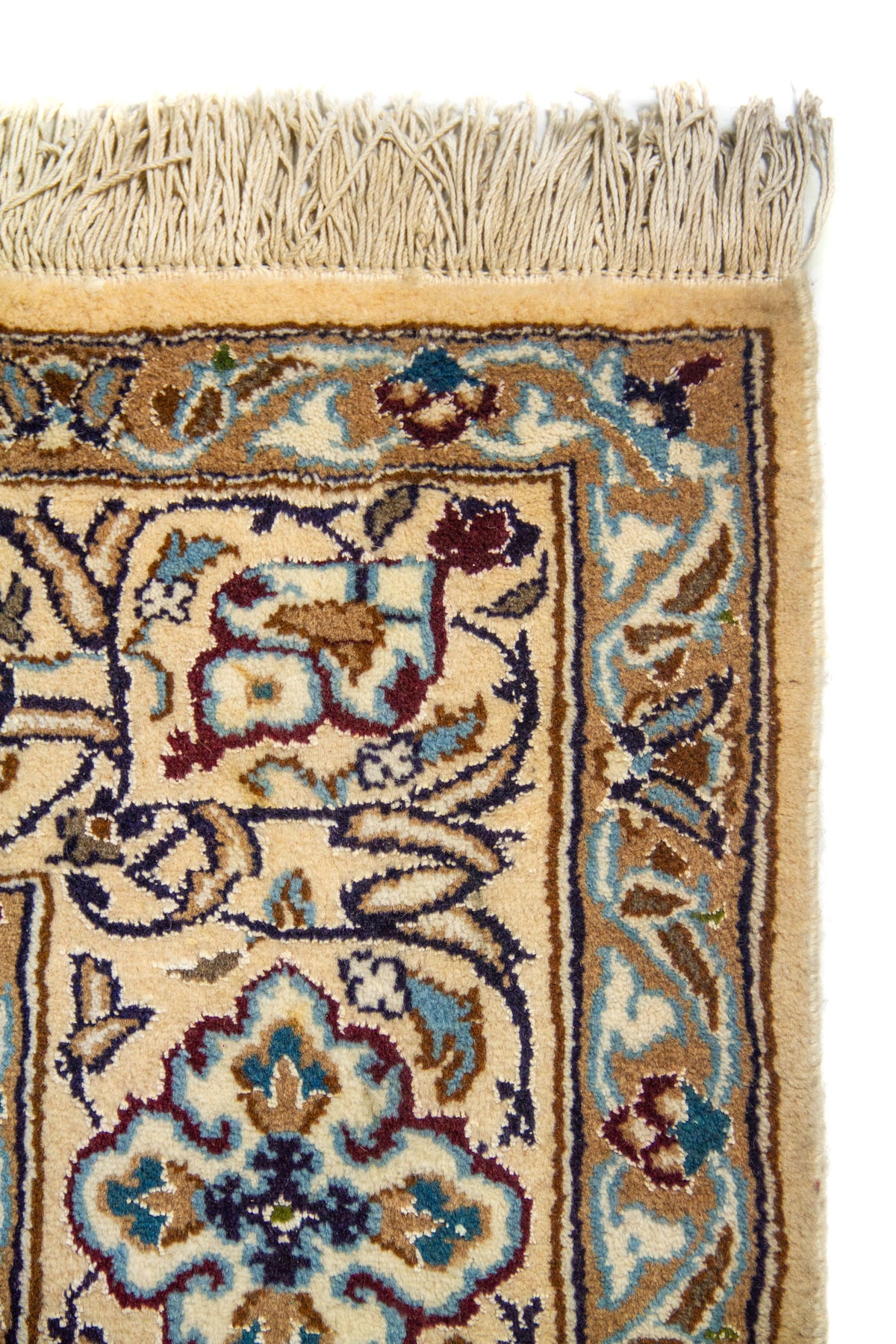 Detalle de esquina de alfombra con flecos color blanco suave y diseño floral ornamental en tonos celeste, azul y beige.