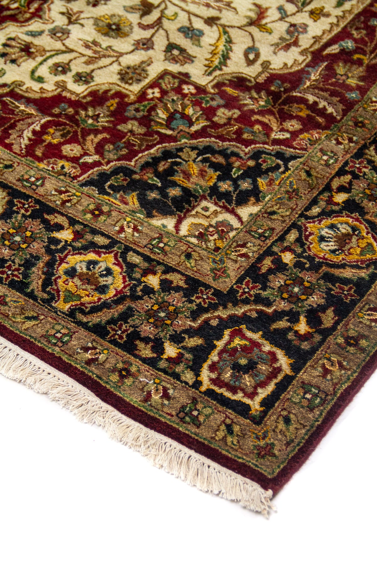 Detalle en perspectiva de esquina de alfombra clásica con fondo blanco suave, bordes oscuros, motivos florales y flecos claros.