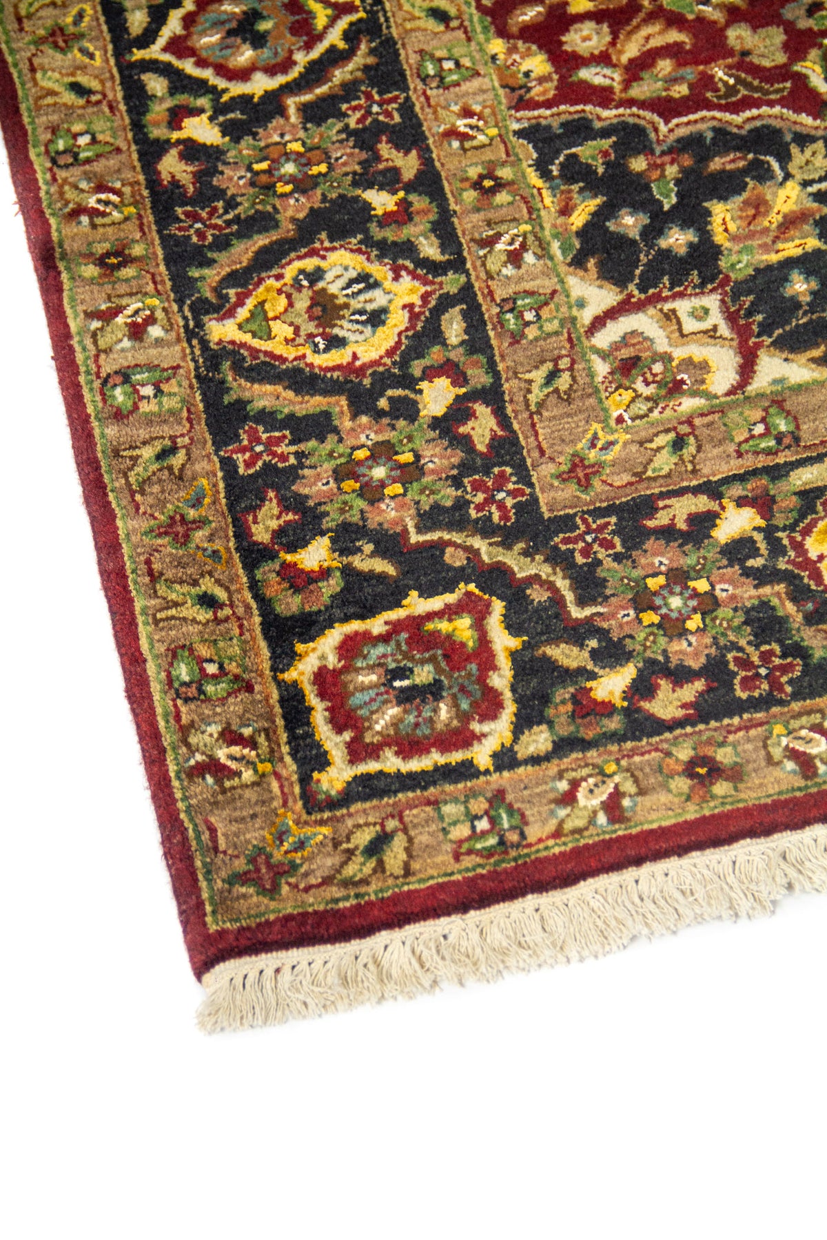 Primer plano de borde de alfombra oriental con guarda negra decorada, detalles florales en beige y rojo, y acabado con flecos.
