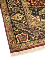 Primer plano de borde de alfombra oriental con guarda negra decorada, detalles florales en beige y rojo, y acabado con flecos.