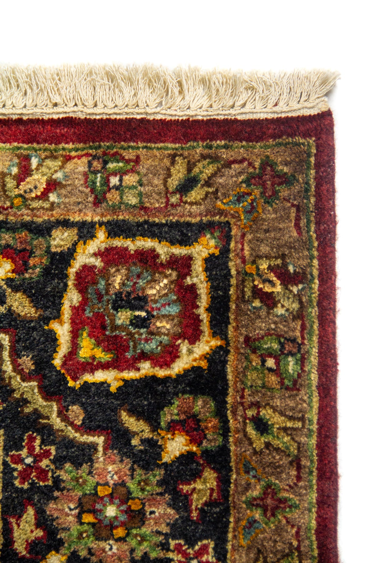 Detalle de esquina de alfombra con marco rojo oscuro y negra, motivos ornamentales y flecos beige.