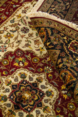 Detalle de alfombra doblada mostrando el reverso del tejido, el borde decorado y los motivos florales en tonos blanco suave, rojo oscuro y negro.