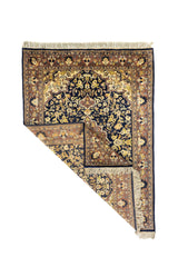 Alfombra rectangular de estilo oriental con una esquina doblada que muestra el reverso del tejido, los flecos y el detalle del borde floral