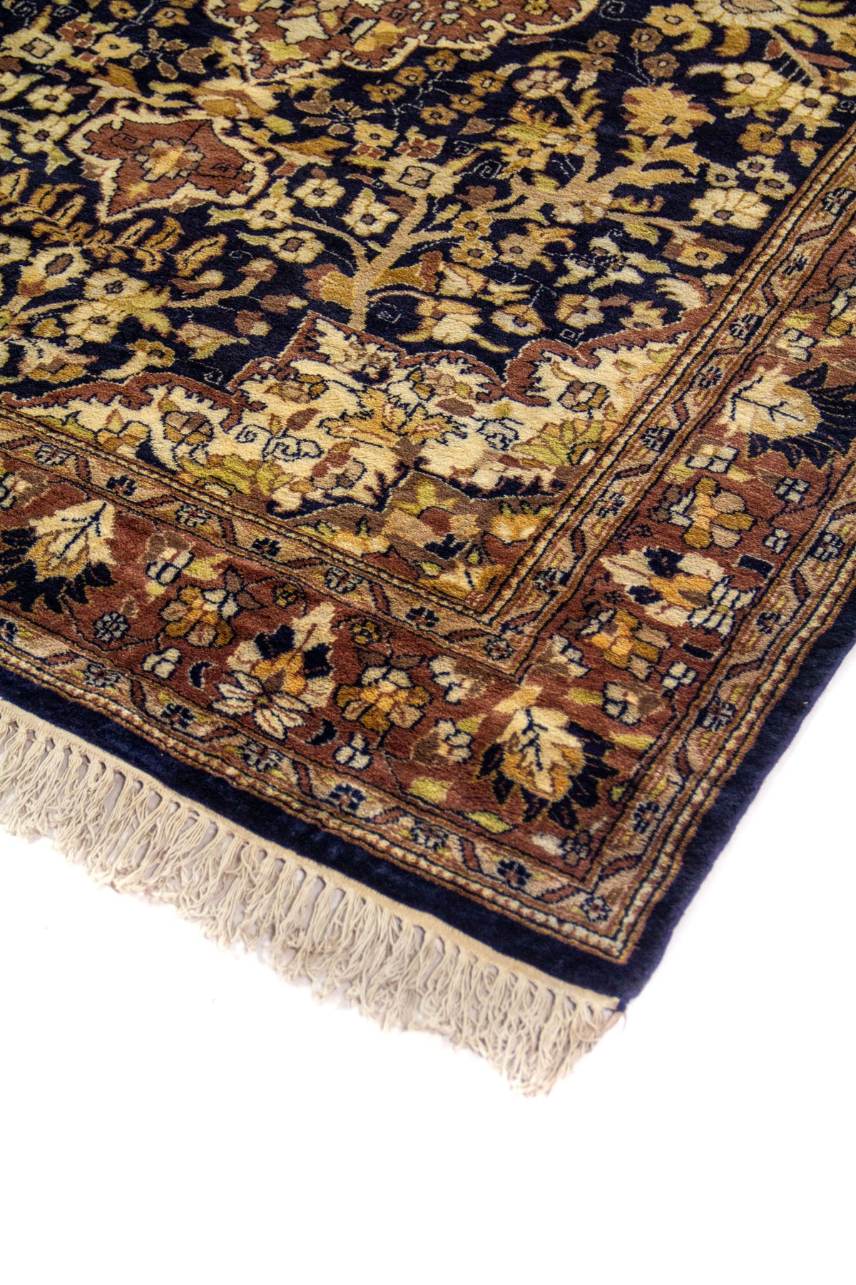 Detalle de esquina de alfombra tradicional con fondo azul oscuro, motivos florales ornamentales y flecos beige