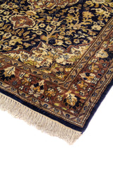 Detalle de esquina de alfombra tradicional con fondo azul oscuro, motivos florales ornamentales y flecos beige