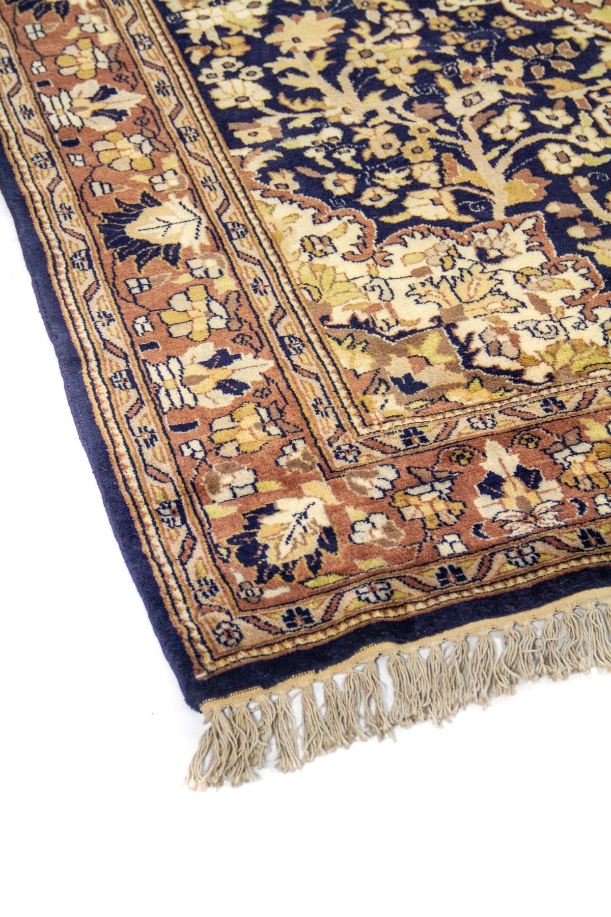 Primer plano lateral de alfombra clásica con diseño floral en tonos beige, café y azul marino sobre borde decorativo