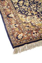 Primer plano lateral de alfombra clásica con diseño floral en tonos beige, café y azul marino sobre borde decorativo