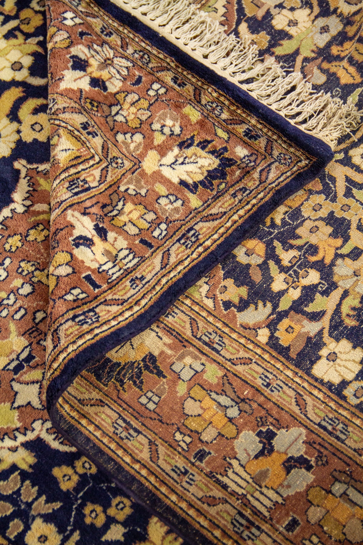 Detalle de alfombra doblada mostrando la textura del tejido, el reverso y los patrones florales del borde y campo central