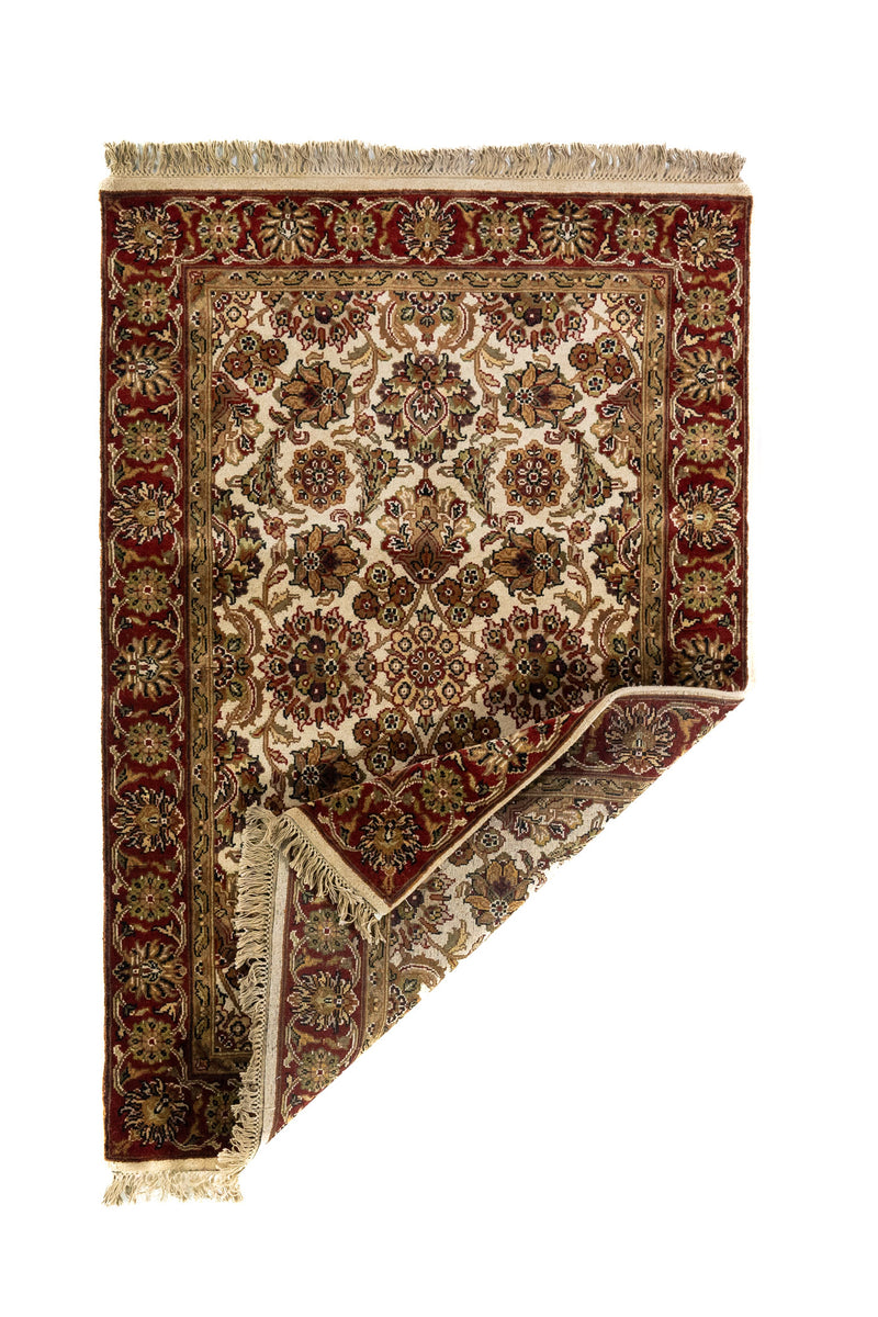 Alfombra clásica floral con una esquina doblada que permite ver el reverso, los flecos y la estructura de su tejido.