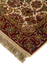 Detalle en esquina de alfombra ornamental con fondo beige, bordes rojos y motivos florales tradicionales